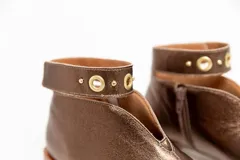 Botín de cuero color borgoña con taco bajo, corte en V en el empeine, pulsera con detalles metálicos y cierre lateral.