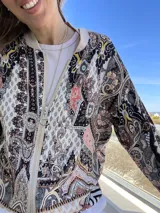 Campera bomber estampada con motivos arabescos en tonos beige, negro, rosa y celeste. Tiene cuello, puños y ruedo acanalados en color beige, cierre frontal con cremallera metálica y bolsillos laterales.
