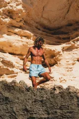 Short de baño celeste con estampado de hojas y flores en tonos naranja, verde y gris. Tiene elástico en la cintura, tres bolsillos y logo de la marca en la parte trasera.