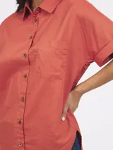 Camisa color coral de lino y algodón, con cuello clásico, mangas cortas con dobladillo y bolsillo de parche en el pecho. Cierre frontal con botones de madera.