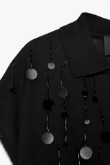 Jersey negro de punto con cuello solapa, manga corta y detalle de lentejuelas plateadas y negras.