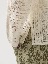 Sweater color crudo tejido a crochet con diseño de cuadrados y círculos, cuello camisero, mangas largas y cierre frontal con botones.