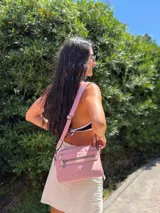 Bandolera color rosa viejo con detalles en cuero marrón claro, múltiples cremalleras metálicas y herrajes plateados. Incluye correa ancha ajustable con el logo de la marca.