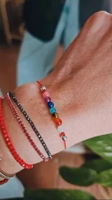 Pulsera de hilo rojo ajustable con siete cuentas de colores representando los chakras y separadores plateados.