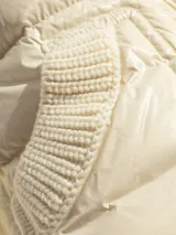 Chaqueta puffer color crema con relleno de plumas, cuello alto de lana y bolsillos delanteros con ribete de lana.