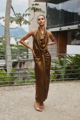 Vestido midi color marrón de satén, con cuello halter fluido y espalda descubierta. Presenta un nudo en la parte delantera, abertura frontal y cierre trasero con cremallera oculta.