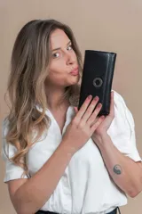 Billetera larga de símil cuero color negro con solapa y aro metálico. Tiene reparticiones con cierre, compartimentos con tarjeteros y bolsillos, monedero con cierre y solapa trasera con botón.