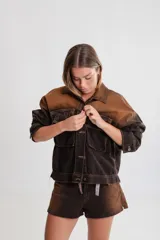 Campera de denim marrón con efecto degradado, corte boxy, cuello camisero, cierre frontal con botones metálicos, mangas largas con puños abotonados, dos bolsillos frontales con solapa y parche con logo en el frente.