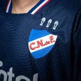 Camiseta de fútbol Umbro del Club Nacional de Football, modelo Away 2 2025. Diseño azul marino con patrón de ondas en azul oscuro, detalles en rojo, escudo bordado, sponsors oficiales y logo Nacional del Mundo en la nuca.