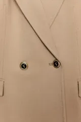 Blazer cruzado color beige, de manga larga, con cuello solapa y forro interior negro. Presenta cierre frontal con botones dorados y bolsillos de vivo en el pecho y bolsillos con solapa en el delantero.