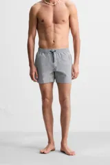 Short de baño con textura seersucker a rayas verticales azul marino y blanco. Tiene cintura elástica ajustable con cordón, bolsillos frontales y traseros, aberturas laterales en el bajo y forro interior.