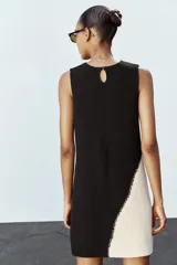 Vestido corto de punto negro con panel lateral color crema, de cuello redondo y sin mangas.