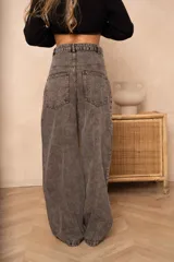 Pantalón jean gris de corte holgado, con cintura media, costuras redondeadas delanteras y traseras, y pliegues en la pierna.