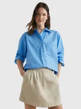 Camisa celeste de popelín de algodón orgánico, corte oversize con hombros caídos, cuello inglés, bolsillo de parche en el pecho y logo bordado en la manga.
