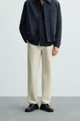 Pantalón chino color beige, corte recto, con bolsillos laterales y traseros. Cierre frontal con cremallera y botón.