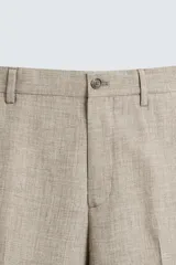 Pantalón de vestir para hombre, color beige claro con textura de tejido de lana. Presenta un corte regular fit, con pliegues marcados en el frente, bolsillos laterales y bolsillos traseros de doble vivo con botón.