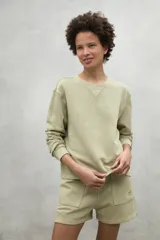 Buzo color verde claro, de corte clásico, con cuello redondo y puños acanalados. Confeccionado en 50% algodón reciclado y 50% algodón orgánico.