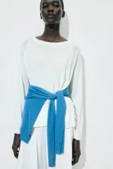 Jersey de punto liso, color azul brillante, con cuello redondo y manga larga. Presenta acabados en rib en puños, cuello y bajo, con aberturas laterales en el ruedo.