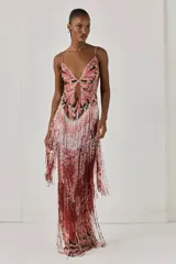 Vestido largo ajustado sin mangas, forrado de tul. Presenta un estampado exclusivo, bordado de cuentas en el busto y el corpiño, abertura en el centro delantero, flecos de cuentas, tirantes finos cruzados y cierre de cremallera invisible en la espalda.