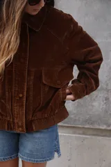 Campera estilo bomber o trucker de color mostaza/naranja quemado con efecto acid wash o desgastado. Presenta cuello camisero, cierre frontal y puños y cintura ajustados con elástico. Posee bolsillos frontales con solapa y botón.