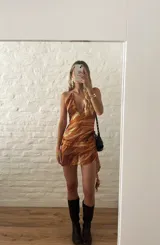 Vestido corto con estampado abstracto en tonos naranja, blanco y marrón. Diseño con escote halter y falda con volados.