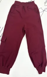 Jogging estilo cargo de felpa color bordó, con cintura elástica, bolsillos laterales y un bolsillo cargo con solapa en la pierna izquierda. Los tobillos tienen puños elásticos.