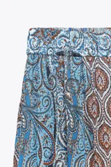 Falda larga de tiro alto con cintura ajustable con lazada y bajo con volantes. Estampado con motivos paisley en tonos celeste, azul y marrón.