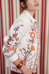 Chaqueta color crudo con bordados de flores azules y naranjas.