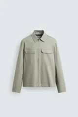 Sobrecamisa color arena de corte relaxed fit, confeccionada en tejido con mezcla de algodón. Tiene cuello solapa, manga larga con puños abotonados, bolsillos de plastrón con solapa en el pecho y bolsillos laterales en la costura de la cadera. El cierre es frontal con cremallera.