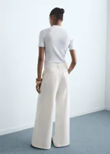 Pantalón de jeans estilo wideleg, color blanco crudo, tiro medio, con cierre de botón y cremallera, y detalle de pinzas delanteras.