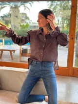 Camisa marrón de algodón con cuello clásico, cierre frontal con botones dorados, mangas largas abullonadas con puños elásticos y corte holgado.