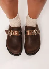 Zuecos marrones de cuero con hebilla metálica ajustable y plataforma baja.