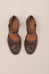 Zapato marrón de cuero vacuno trenzado a mano, con correa al tobillo con hebilla negra y suela de cuero.