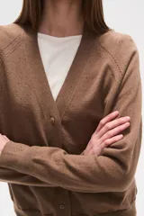 Cardigan de punto color blanco roto con motas oscuras, de manga larga y escote en V con cierre de botones frontales.