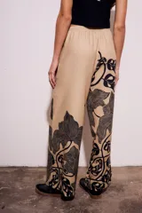 Pantalón de lino color beige con estampado de hojas negras, corte flare y tiro alto.