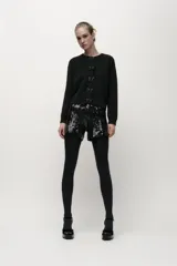 Chaqueta de punto negra con cuello redondo y manga larga. Presenta detalle de lazos con abalorios en el frente y cierre con botones a presión.