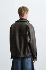 Cazadora bomber de efecto piel color marrón oscuro, con cuello solapa, cierre frontal de cremallera, bolsillos de vivo en cadera y bajo elástico.