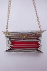 Cartera tipo sobre color beige con textura granulada y correa de cadena dorada.