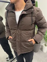 Campera puffer marrón de nylon impermeable con capucha forrada con corderito desmontable, cierre frontal con cremallera y broches a presión, y bolsillos laterales con cierre.