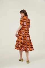 Vestido midi con estampado abstracto en tonos marrón, naranja y rosa. Tiene cuello camisero, mangas cortas abullonadas y falda escalonada con volantes.