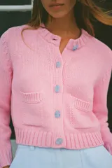 Chaqueta de punto rosa con cuello redondo y manga larga. Tiene bolsillos delanteros y cierre frontal con botones celestes.
