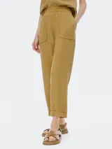 Pantalón de tiro alto color mostaza, de corte recto y largo al tobillo con puño doblado. Presenta cintura elástica y bolsillos delanteros con tapa redondeada.