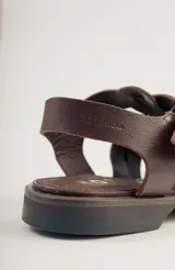 Sandalias bajas de cuero marrón con tiras entrecruzadas y hebilla dorada.