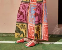 Sandalias bajas con base de cuero y capellada tejida a crochet con rayas horizontales en tonos rosa, naranja y amarillo. La base está ribeteada con hilo de crochet verde.