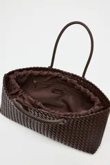 Bolso shopper alargado color marrón chocolate con diseño trenzado. Tiene doble asa de hombro y cierre superior con botón imantado. Incluye una bolsa interior con cierre fruncido.