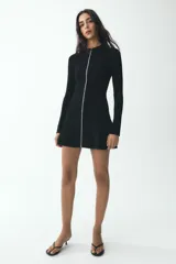 Vestido corto negro de punto con cuello redondo y manga larga. Presenta cierre frontal con cremallera metálica.