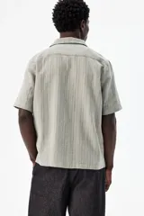 Camisa de manga corta color verde claro, confeccionada en mezcla de lino y algodón. Tiene cuello abierto, tapeta lisa, bolsillo superior y canesú en la espalda.