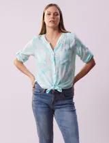 Blusa celeste con estampado cachemir blanco, de gasa, con cuello a la base, escote en v y abertura con botones. Tiene bolsillos en el pecho, mangas 3/4 regulables con presilla y botón, y terminación de ruedo con nudo.