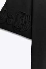 Camiseta negra de algodón con cuello redondo, manga corta y detalle de flores con volumen en las mangas.