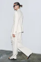 Blazer color blanco confeccionado en algodón, con cuello solapa de muescas y manga larga. Tiene bolsillos con solapa en delantero, forro interior a tono y cierre frontal con botones metálicos en relieve.